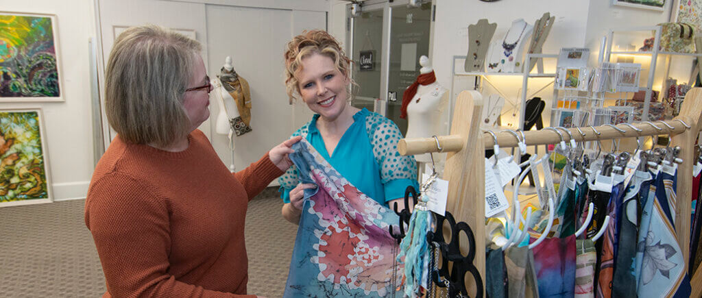 Carrie Wright (L) shows Angie Hibner (R) some of her handpainted silk scarves. Photo by Mike Rhodes